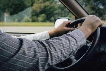 A driver in a business shirt with hands on a steering wheel and road background commuting, going to...