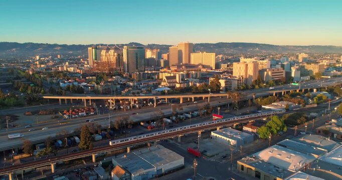 Aerial view of Oakland, California, USA, at sunrise. Cars travel on the highway below the city skyline, showcasing urban life and transportation.