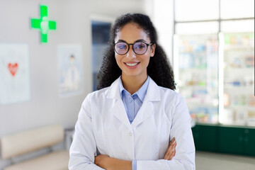 Portrait of professional female pharmacist wearing lab coat and glasses, smiling at camera with...