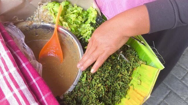 A close-up of a person preparing Pecel Semanggi, a traditional Indonesian dish made of water clover, with a ladle to mix the ingredients.
