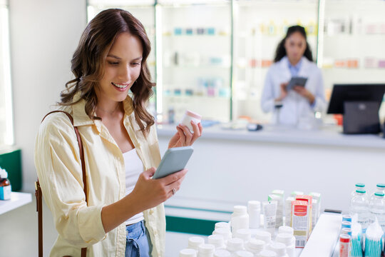 Young European woman using cellphone and holding jar of pills and looking for information of medicine in drugstore - Powered by Adobe