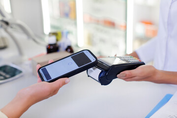Pharmacist and customer using NFC smartphone with contactless payment terminal to buy prescription medicine, health care goods, closeup