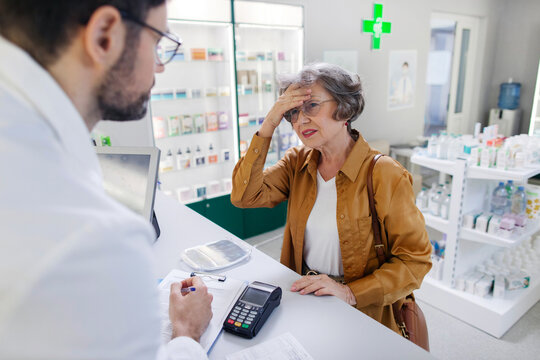 Senior woman talking and consulting with pharmacist, touching head, suffering from headache, male worker offering medicaments - Powered by Adobe