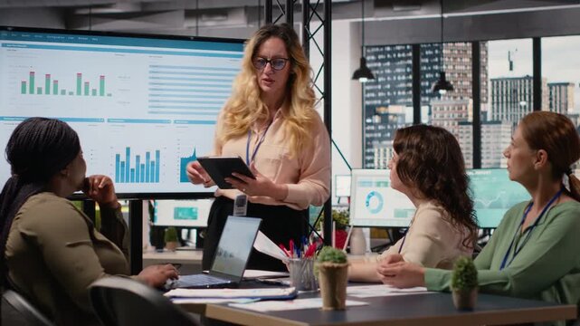 General director hosting a briefing session with her team to present data driven reports, pointing at the screen to examine business productivity. Professionals embody strategic thinking. Camera B.