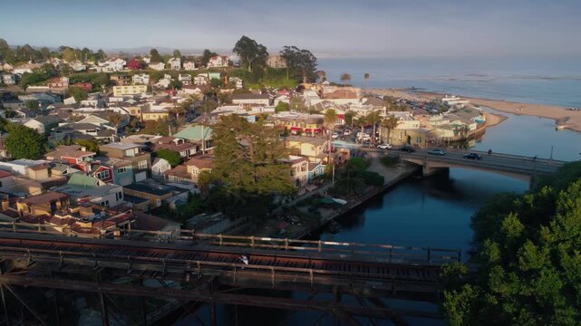 Aerial view of Capitola Village in California, USA. Two people sit on a bridge, enjoying the view of the colorful houses and the ocean.