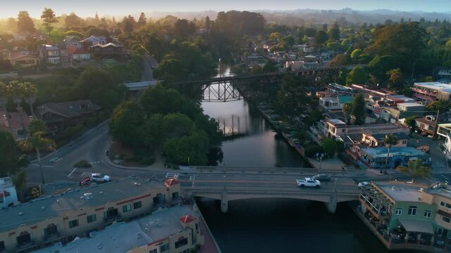 Aerial view of Capitola Village in California, USA, at sunrise. A white car crosses the bridge over the river, connecting the colorful buildings.