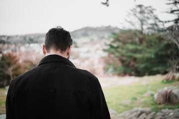 Confident young Hispanic man using a smartphone in the park, wearing a black jacket