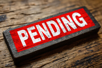 A wooden block with the word pending in white letters on a red background placed on a wooden surface