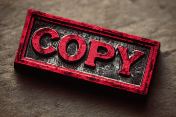 Close up of a red copy stamp with black background on a textured surface in a horizontal format