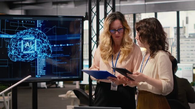 Powerful team of associates review AI generated analytics from TV monitor, applying machine learning tools and neural networks to drive development and achieve corporate goals. Camera B.
