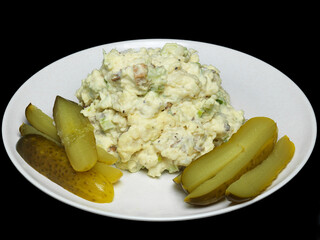 Potato salad with dill pickle spears on a white plate