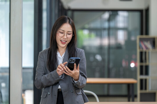Smiling asian businesswoman using smartphone in modern office: browsing internet, checking email, and accessing business information