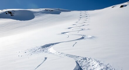 Obraz premium Photo of fresh ski tracks winding down a snowy mountain slope under a clear blue sky