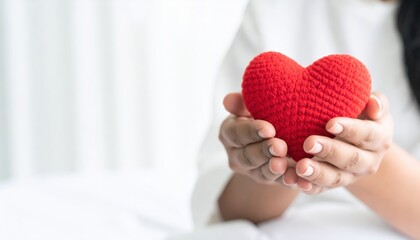 Fototapeta premium A person holds a red crocheted heart, symbolizing love and affection, against a softly blurred background.