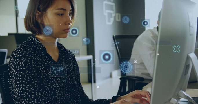 Typing female office worker in patterned top analyzing at office, with monitors keyboards overlays