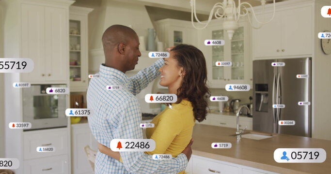Hugging couple standing at home kitchen island, displaying floating social media notification icons - Powered by Adobe