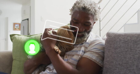 Smiling senior man wearing shirt holding long-haired dog on couch in living room, with chat overlay