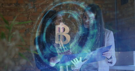 Examining two women in blazers reviewing folder in modern office, with holographic Bitcoin overlay
