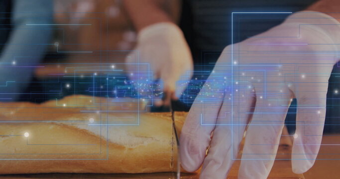 Slicing gloved hands cutting baguette on wooden countertop in kitchen, with digital circuit overlay - Powered by Adobe