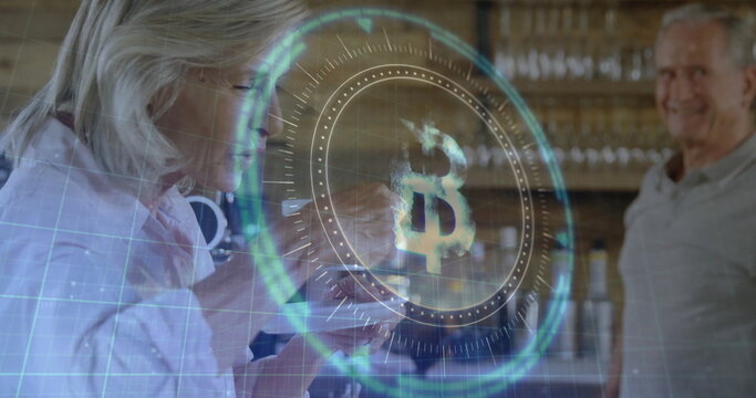Tapping senior woman and smiling senior man examining glowing Bitcoin interface at wooden counter