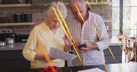 Senior couple reviewing documents and calculating expenses in home kitchen, with smartphone
