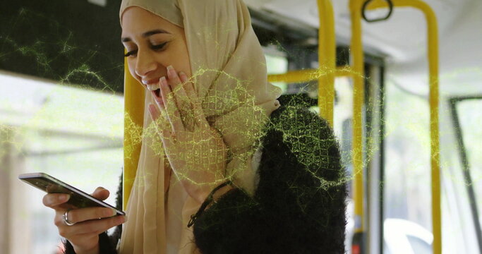 Smiling woman wearing hijab and black jacket, holding phone inside bus by windows with yellow poles - Powered by Adobe