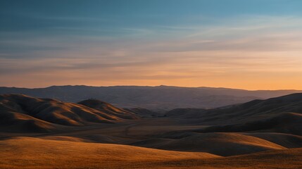 Naklejka premium A serene landscape featuring rolling hills bathed in warm sunlight, showcasing a gradient sky transitioning from blue to soft orange hues during sunset.