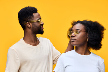 Fototapeta premium Happy young couple wearing sunglasses, with a vibrant yellow background, showcasing love and connection through playful emotions and stylish fashion
