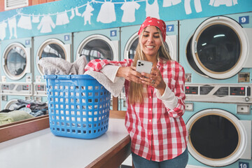 Woman using phone while waiting for laundry, enjoying her free time in a laundromat