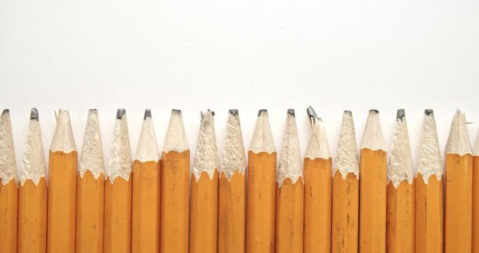 Panning across row of used and worn out yellow pencils with broken pencil tips, with one single and unique sharpened pencil.