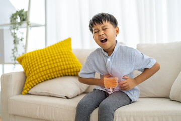 Portrait of sick unhappy little child asian boy touching belly stomach with suffering from stomach...