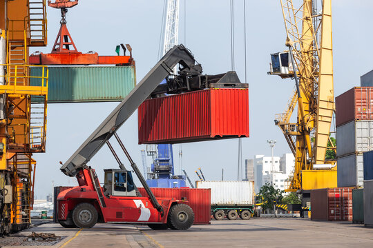 A container yard with stacked cargo containers and cylindrical tanks, where a reach stacker loads containers for transport, showcasing efficient yard management in global shipping logistics.