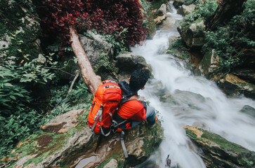 A young man sits on a rock near a mountain river. Beautiful mountain scenery.