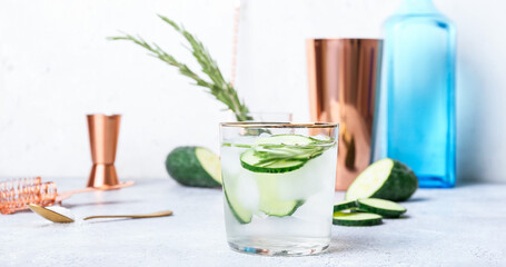 Glass of cold gin tonic and cucumber slices on light background