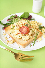 Plate with tasty scrambled eggs sandwich and salad on green background