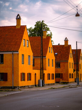Historic yellow houses with red-tiled roofs along Kronprinsessegade in Nyboder, Copenhagen, Denmark, under a partly cloudy sky with street and architectural details.