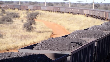 Multiple train wagons of mined manganese ore moving slowly in the South African bush outback.