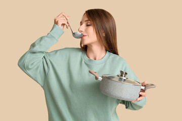 Young woman tasting chicken soup on beige background