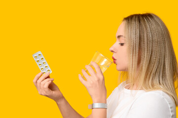 Young woman with vitamin A pills and glass of water on yellow background, closeup