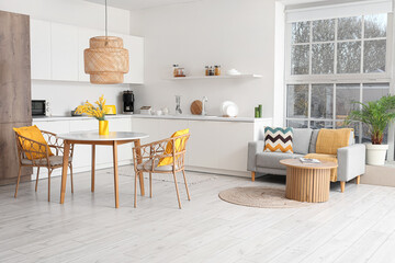 Interior of spacious stylish kitchen studio with table, armchairs, mimosa flowers, houseplant, counters and sofa