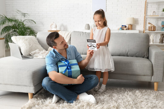 Little daughter giving her father greeting card in living room. Father's Day celebration