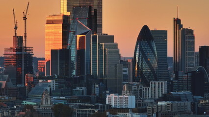 United Kingdom, London: Modern skyscrapers and construction cranes reflecting the vibrant orange and pink hues of a London sunset during twilight. Drone flight