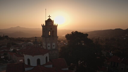 Cyprus: Warm sunset illuminates the bell tower of a church in a picturesque Cyprus village, creating a serene and spiritual atmosphere. Drone flight