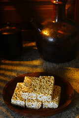 A plate of sweet Brondong, an Indonesian puffed rice snack, is placed on a rough surface next to a traditional earthenware jug in a rustic, low-key setting.