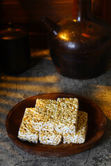 A plate of sweet Brondong, an Indonesian puffed rice snack, is placed on a rough surface next to a traditional earthenware jug in a rustic, low-key setting.