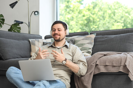 Young male teacher in headphones with laptop giving online lesson at home