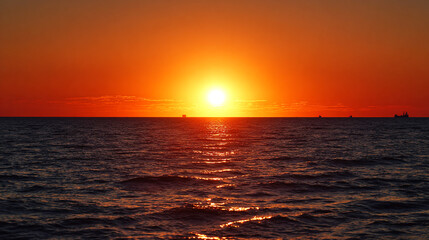 Sunset over the ocean, with an orange sky and a large sun setting behind it.