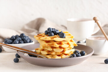 Delicious Belgian waffles with blueberries in plate on table against white background