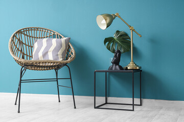 Chair and coffee table with figurine, monstera leaf and desk lamp near blue wall