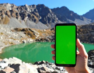 A hand holds a phone with a green screen, showcasing a mountain lake